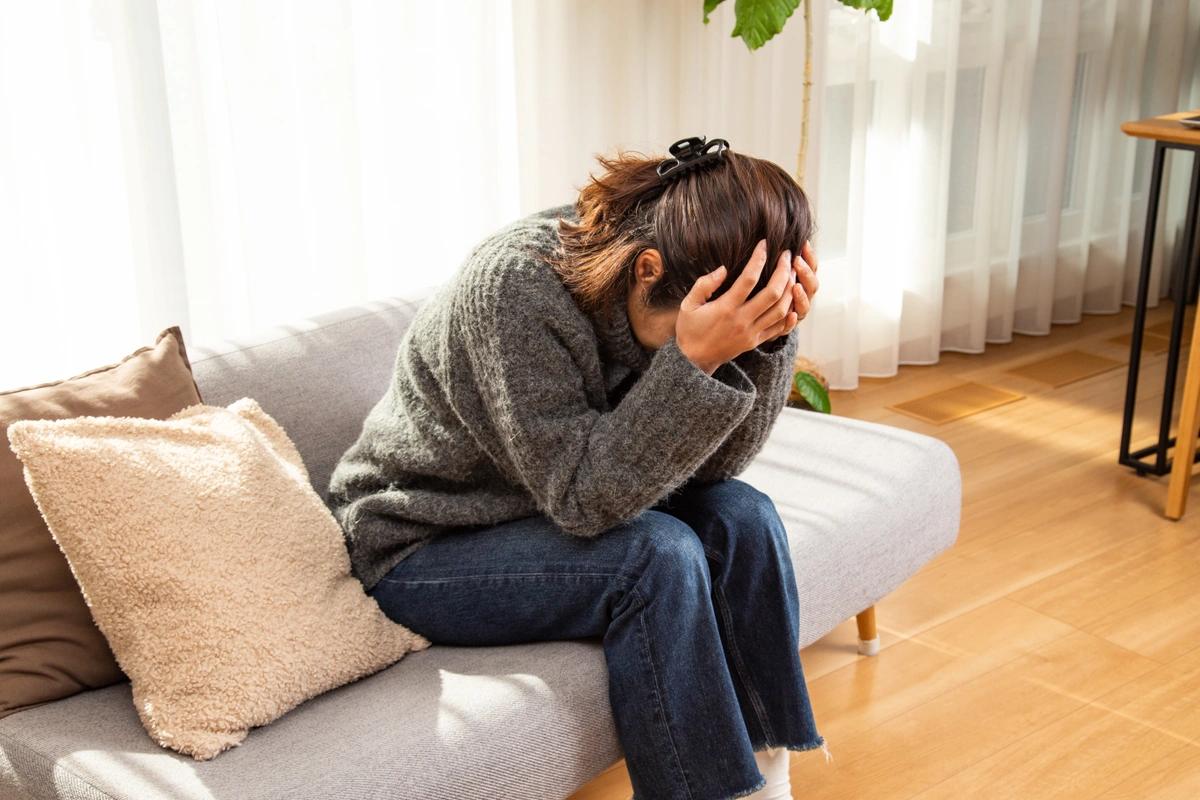 A woman sits on a sofa with her head in her hands