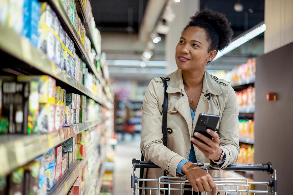 A woman checks the shopping list on her phone as she pushes a trolley round the supermarket