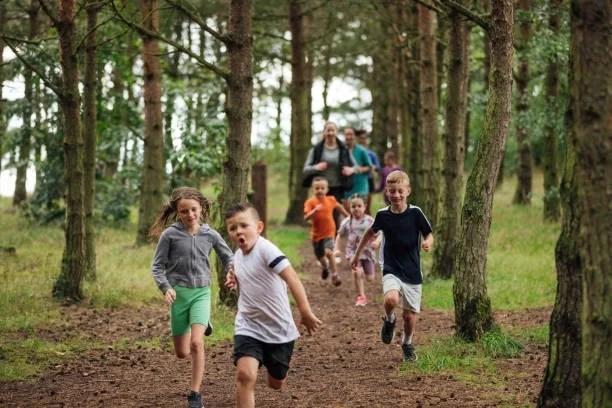 Image of school children running through a forest having fun. Summer school holidays set to get cheaper as government cuts VAT on days out. Universal credit cheap days out. Holiday and Activity Programme (HAF)