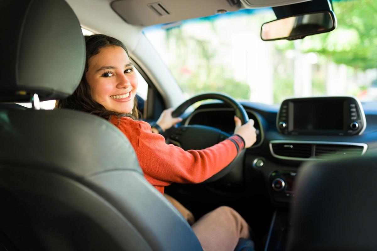 A smiling young woman in the driving seat of her car
