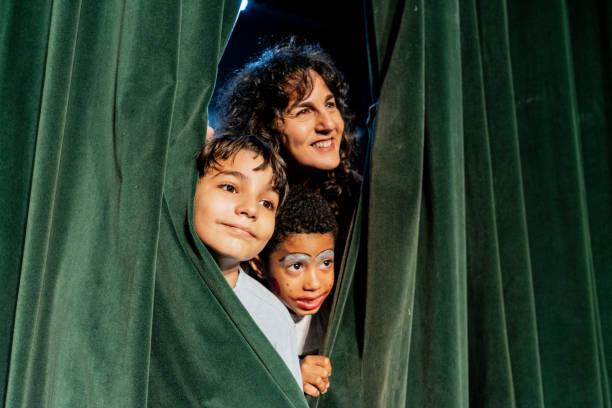 kids looking out of a theatre curtain. Kids go free to top London shows this summer. Kids Week 2025