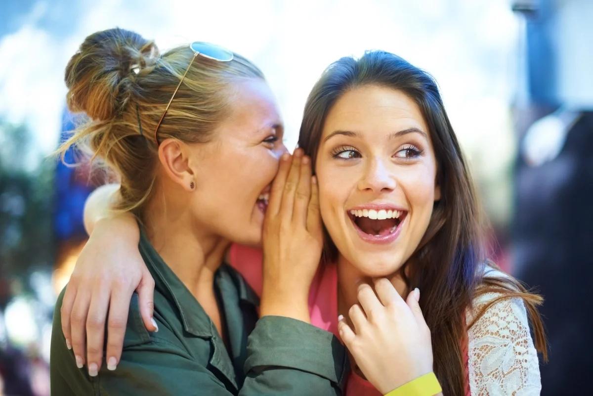 A woman whispers a secret into the ear of her friend