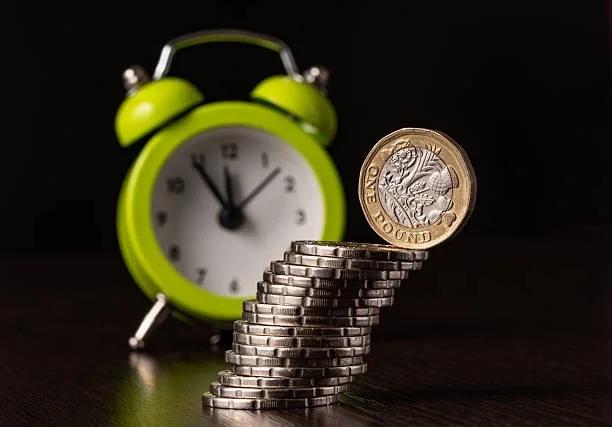 Image of a pile of £1 cons next to a clock. Stuck for cash? 5 safe ways to get emergency money – even with a low credit score