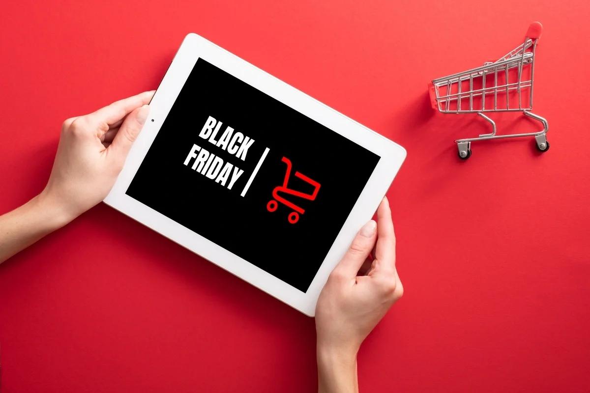Hands holding a framed Black Friday sign with a miniature shopping trolley next to it