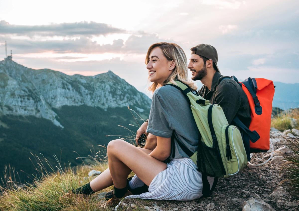 Two hikers sitting atop a mountain smiling and taking in the view