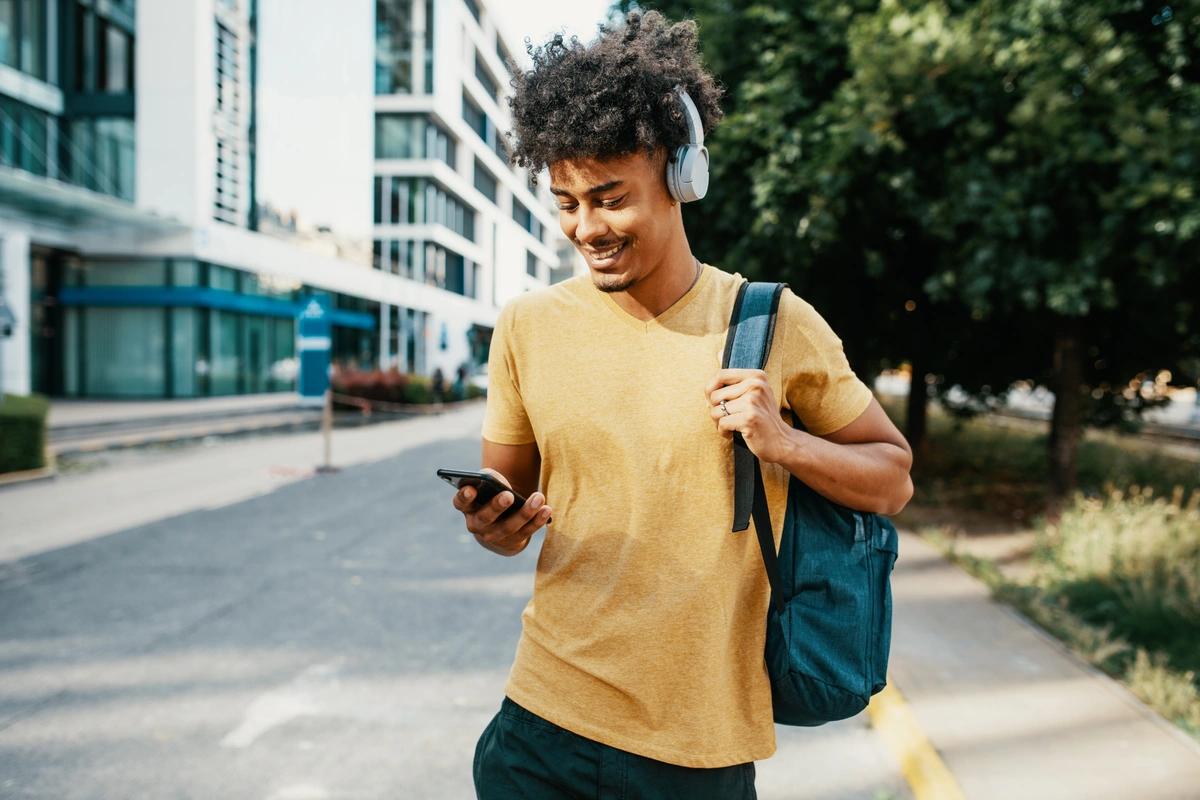 Smiling young man checks his mobile phone as he walks down a street