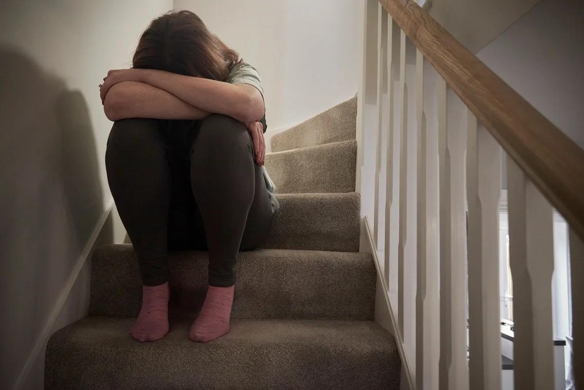 A woman sits on the stairs with her head in her hands