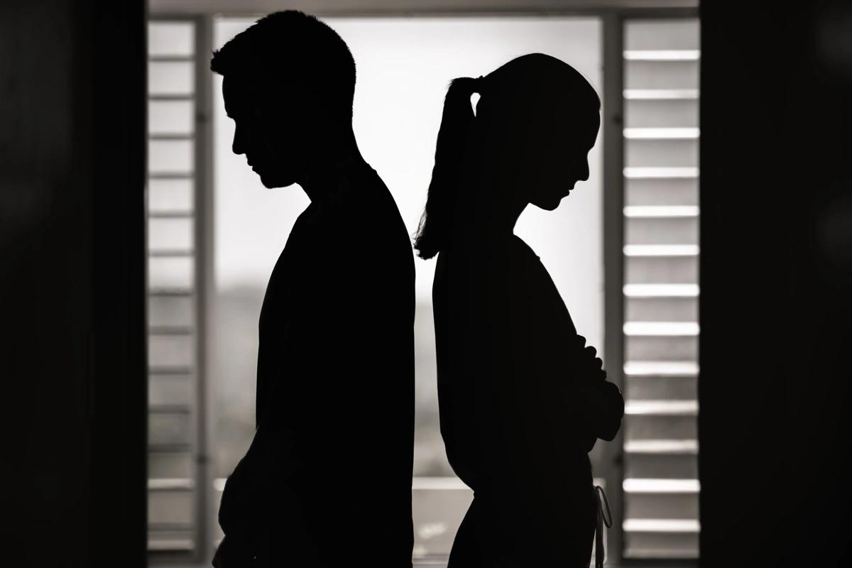 The silhouettes  of a couple standing with their backs to each other