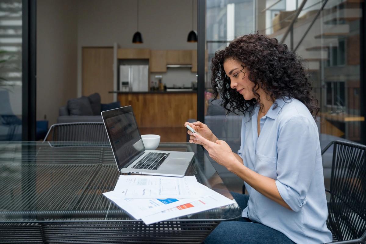 A woman sitting at her laptop checks something on her phone.