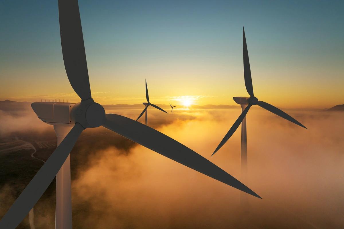 The tops of three wind turbines above the clouds at sunrise