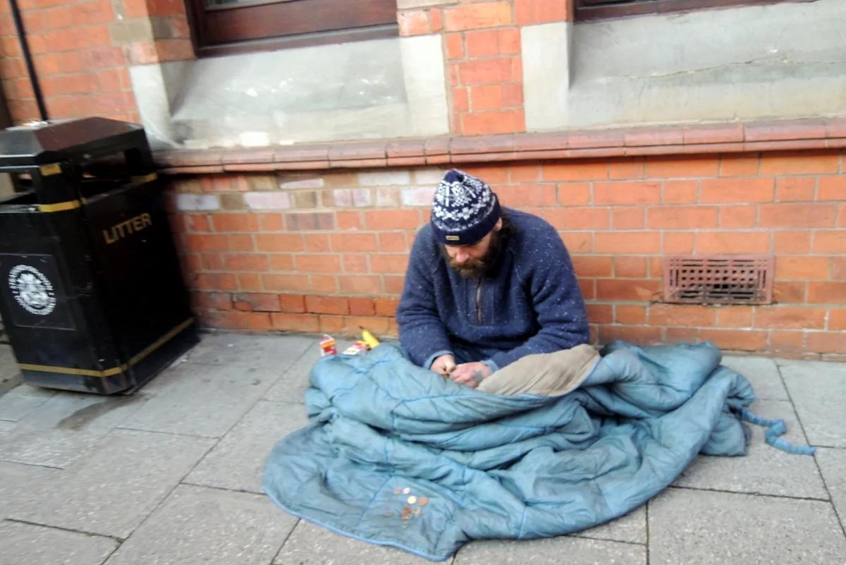 A homeless man sits under a duvet on the pavement